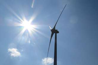 Three-wing wind turbine in front of the sun with a blue sky