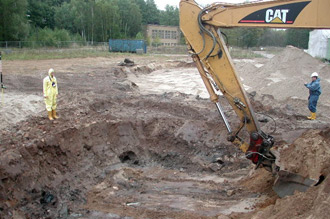 Excavator digging earth from a trench, two men next to it