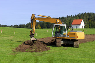 Excavator on field, mound of earth, house in the background