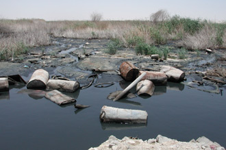 Schwarzes Wasser mit Abfall in Landschaft mit vertrockneten Büschen und Gräsern